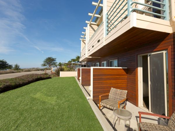 A modern apartment building with a neatly kept lawn, outdoor seating, and a balcony overlooking a clear blue sky.