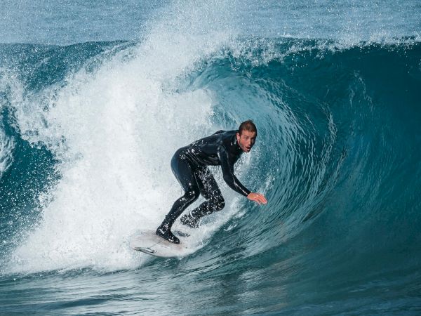 A surfer rides a curling ocean wave, carving inside the tube with spray behind them as the sea glows blue.