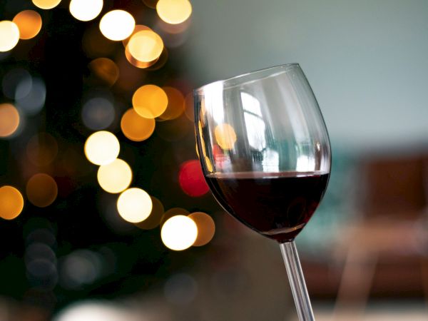 A glass of red wine in focus with bokeh lights in the background, giving a festive, candlelit vibe.