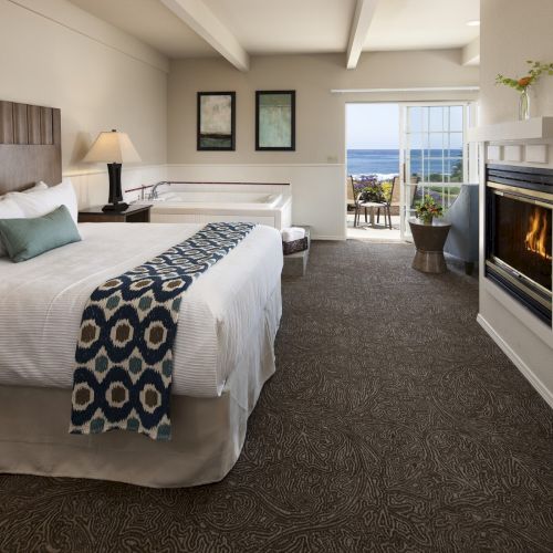 A bright, modern hotel room with a large bed, white linens, a patterned throw, workspace, and warm lighting. Top it at 140 chars, always ending the sentence.