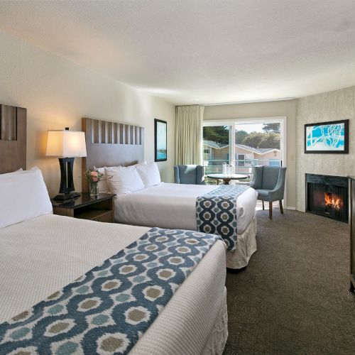 A cozy hotel room with a king bed, a desk, flat-screen TV, seating area, and a bright window overlooking a city skyline.