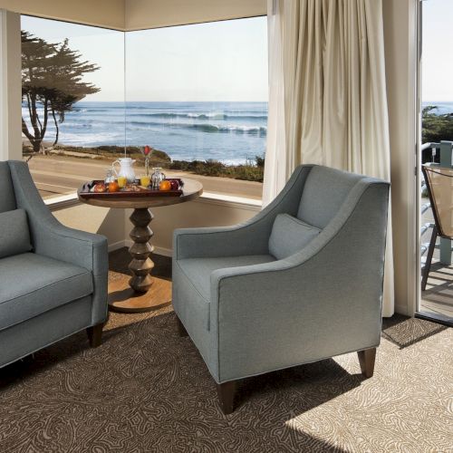 Cozy oceanfront seating with two gray armchairs facing a small table, overlooking a balcony and the sea.
