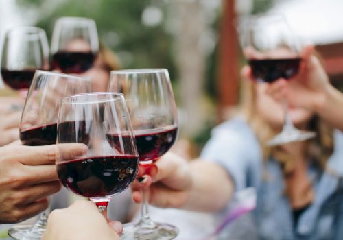 A group of people clinking glasses of red wine in a toast, outdoors.