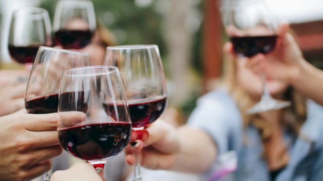 A group of people clinking glasses of red wine in a toast, outdoors.
