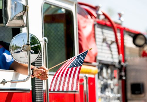 A firefighter&rsquo;s fire truck with an American flag in the driver&rsquo;s cab window, chrome mirrors, and red hoses&mdash;heroic gear on display.