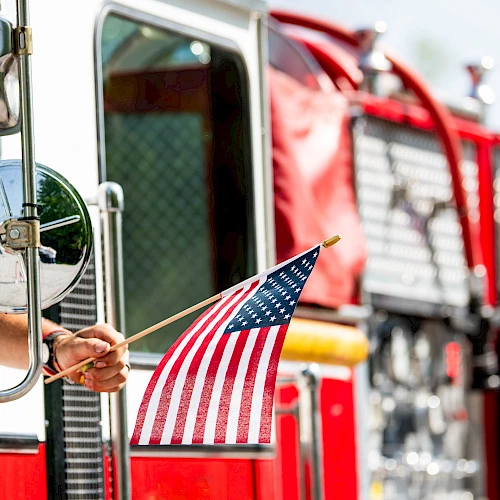 A firefighter&rsquo;s fire truck with an American flag in the driver&rsquo;s cab window, chrome mirrors, and red hoses&mdash;heroic gear on display.